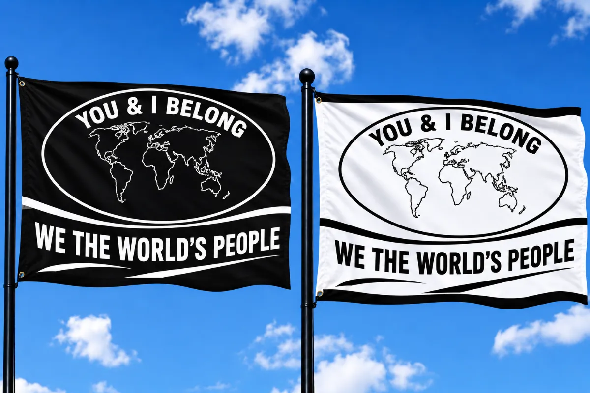 Two large You and I Belong flags, one black and one white, flying side-by-side on flagpoles against a bright blue sky with clouds.