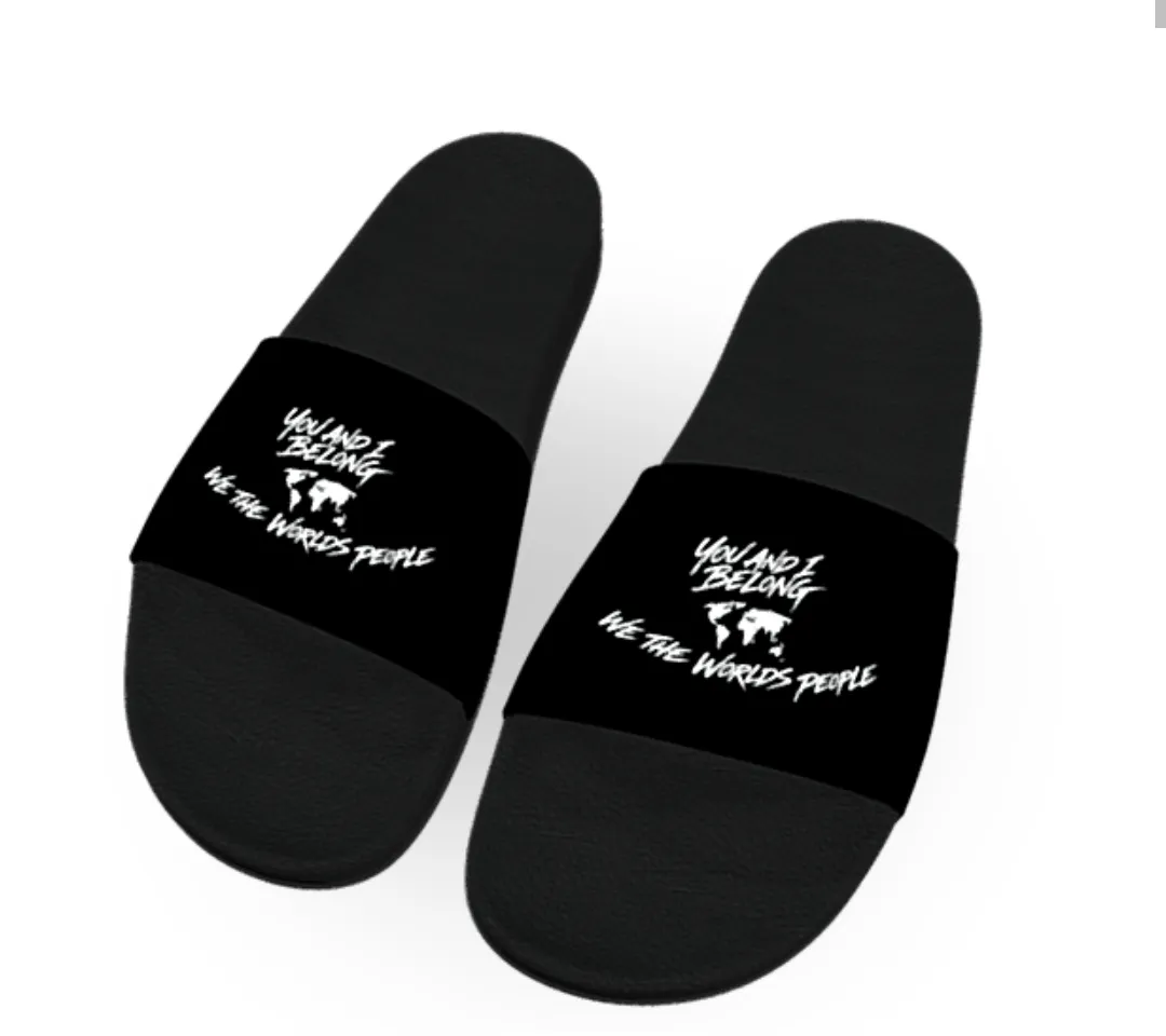 A pair of black slide sandals viewed from above. The straps feature a white world map silhouette with the text "You and I Belong" above it and "We the World's People" below it.