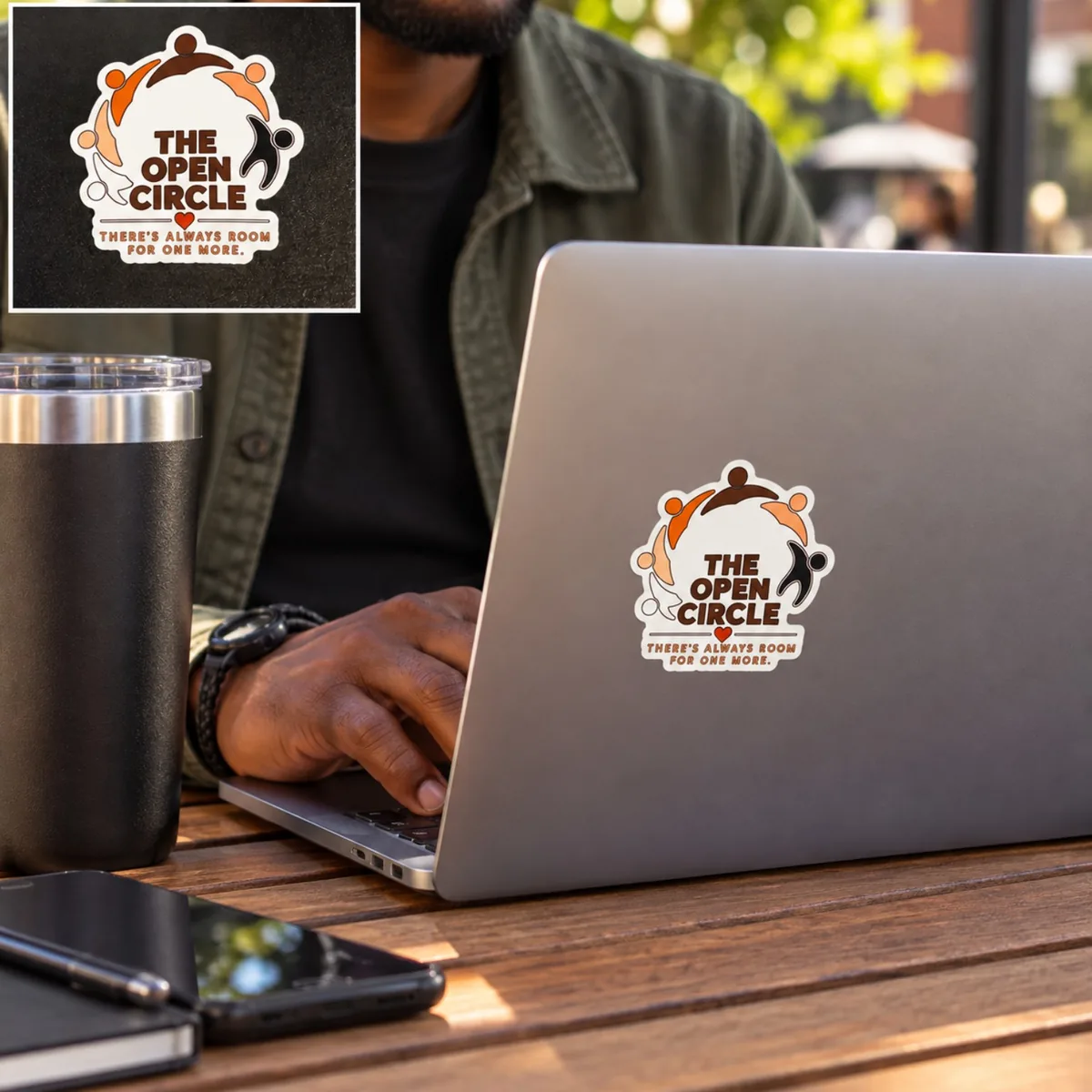 Illustrative lifestyle image: The Open Circle sticker on the back of a laptop being used at an outdoor table