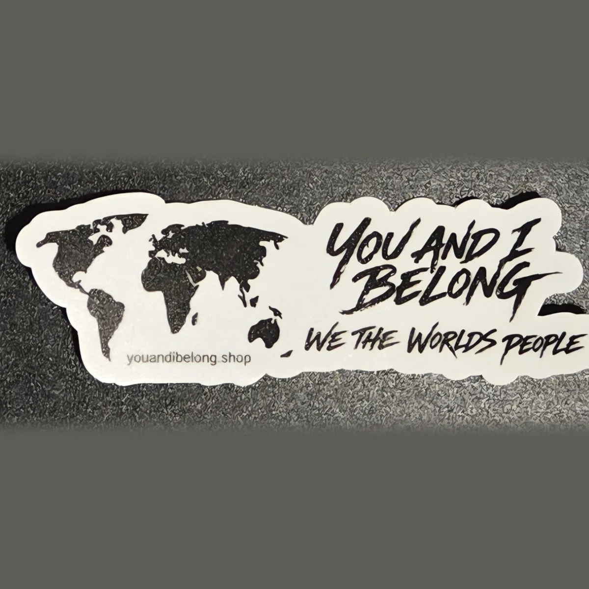 White die-cut You and I Belong sticker with a black world map and the words We The Worlds People